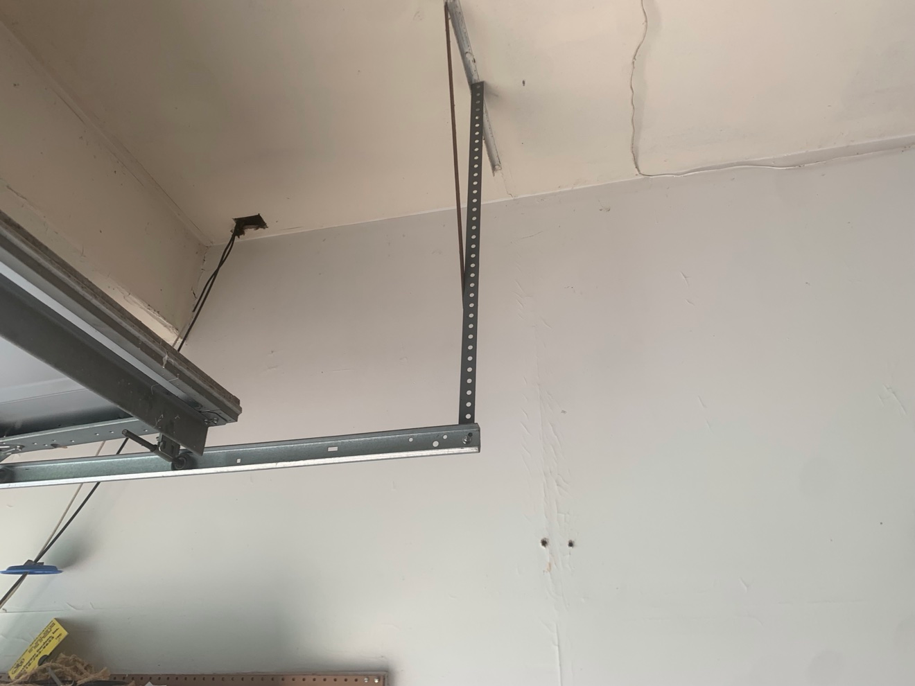 Close-up of garage door opener rail and wall with drywall seams, screw holes, and patch marks before re-taping