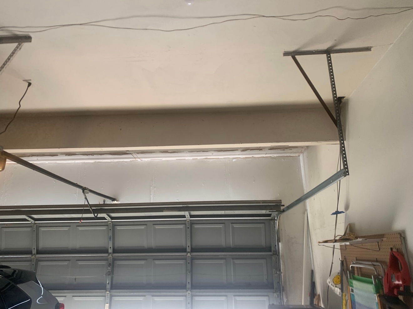 Garage ceiling above closed garage door with fresh joint compound applied over re-taped seams, skim coating in progress