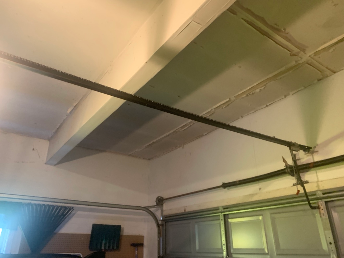 Garage ceiling with old drywall tape peeling off seams around the opener rail, exposing joint areas before re-taping