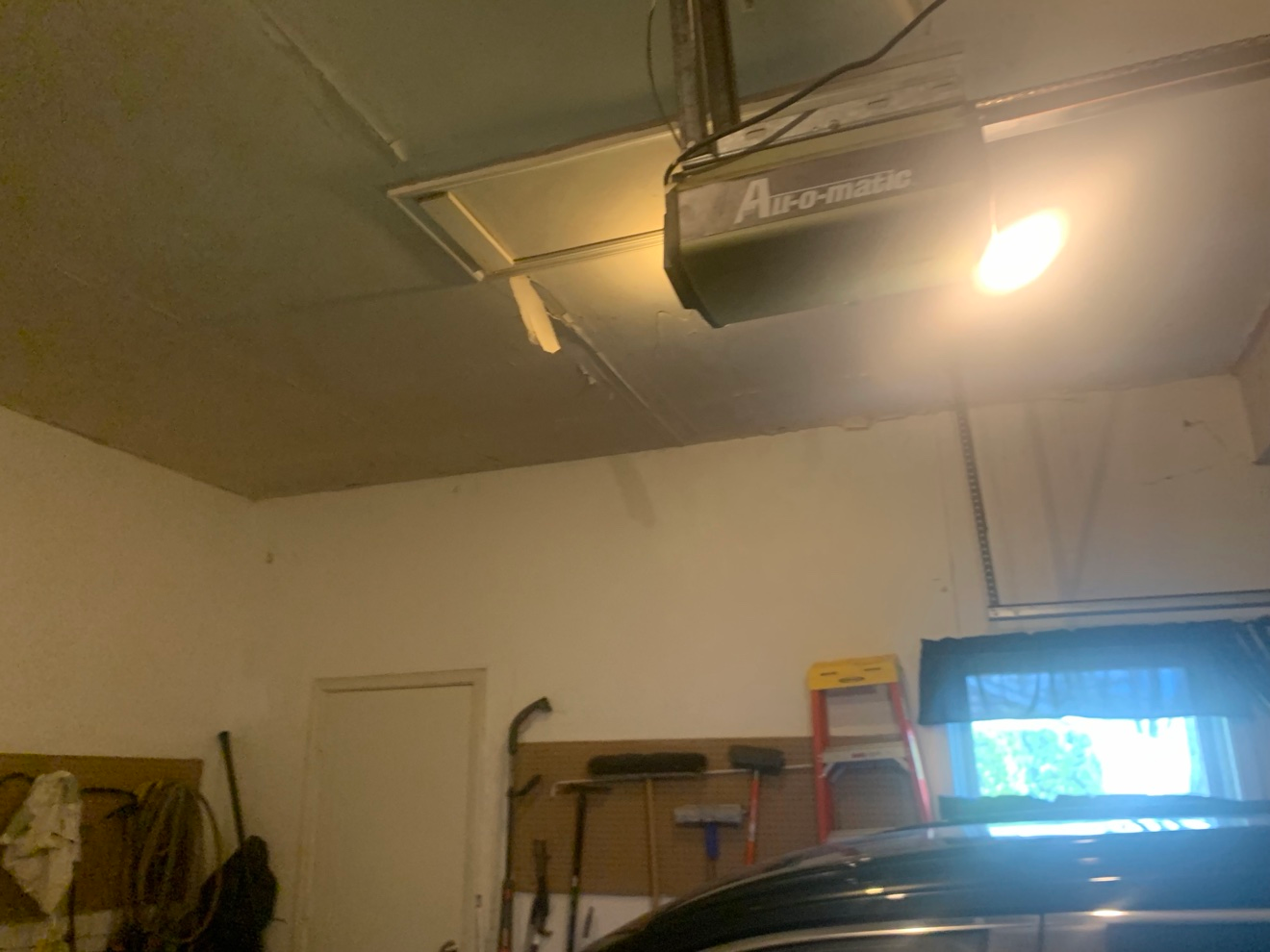 Garage ceiling with a strip of old drywall tape hanging loose near the vent and door opener, before re-taping