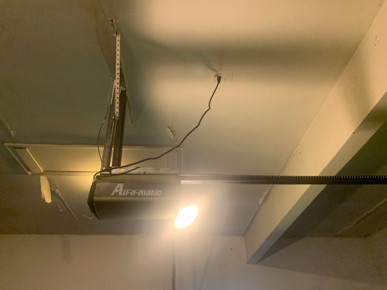 Close-up of garage ceiling with a dangling strip of old tape and compound near the door opener, before re-taping